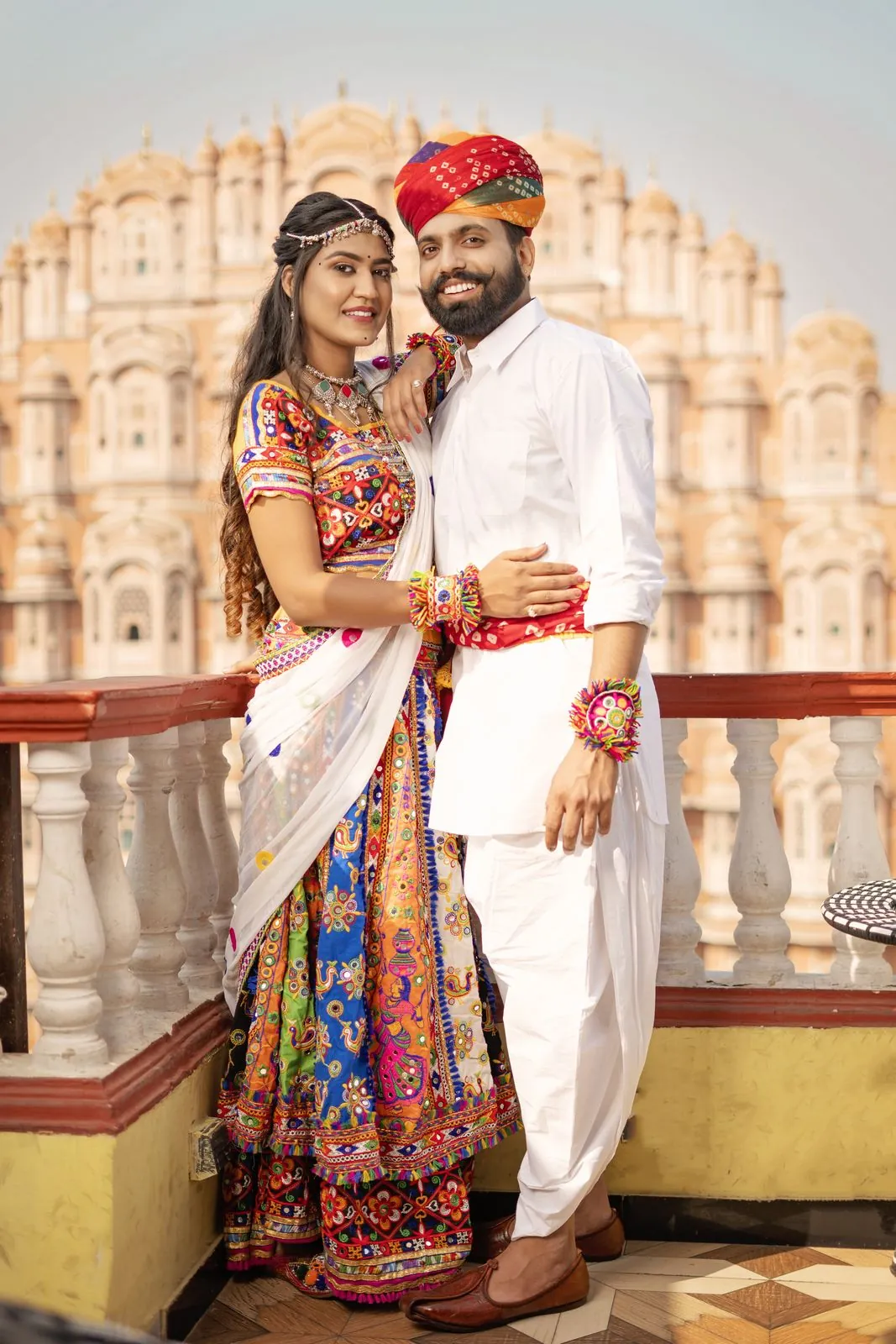 Couple in Rajasthani outfits with a turban on a terrace in front of Hawa Mahal
